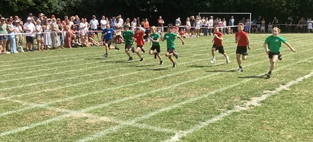 Boys are participating in a running race on the same grassy track. Again, spectators are lined up along the side.
