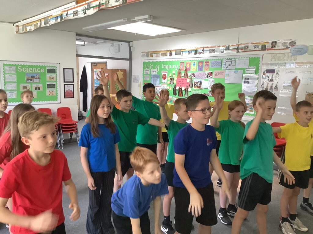 Pupils in Blue, Green and Red PE kits taking part in a ballet lesson in a classroom