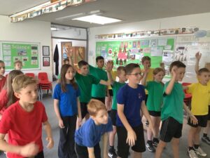 Pupils in Blue, Green and Red PE kits taking part in a ballet lesson in a classroom