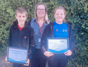 the picture shows a celebration of Leigh Academy Hartley receiving an award for being an "ADHD Friendly School," with an adult and two students proudly displaying the certificates.