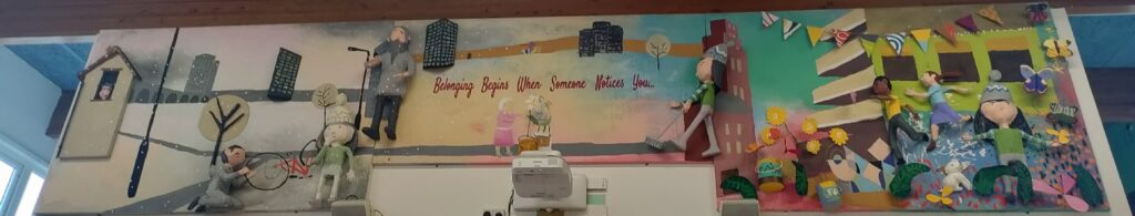 This is a panoramic view of the complete or major part of the wall installation. The mural is divided into distinct thematic sections, likely representing the seasons or different phases of life/community experience.