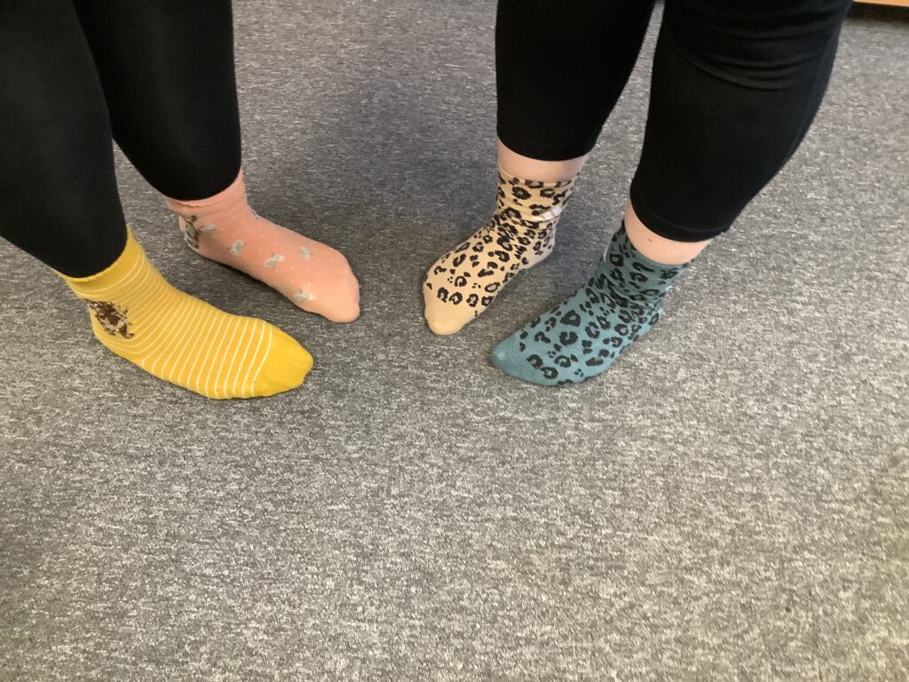 A close-up shot of four feet wearing colorful, patterned socks on a gray carpet.