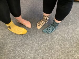 A close-up shot of four feet wearing colorful, patterned socks on a gray carpet.