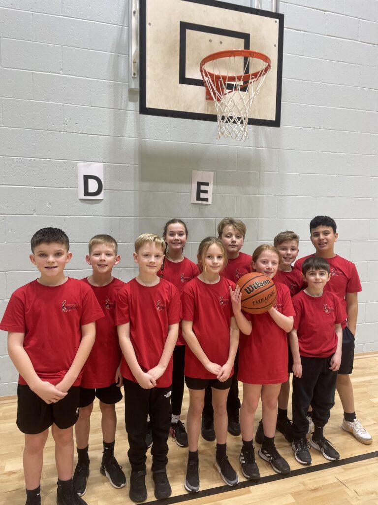 A young basketball team, dressed in red pose for a picture on the court