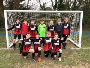 a junior football team wearing red and black pose for a picture in front of a goal. The keeper is wearing green