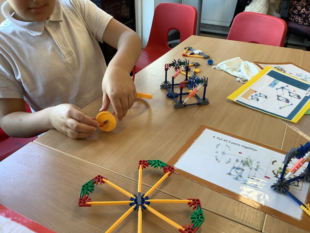 A student uses their hands to assemble a gear system from a colorful building kit on a classroom desk.