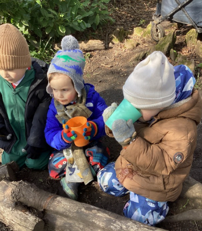 Three children wearing woolly hats and gloves drinking from plastic cups