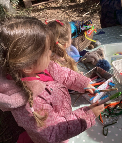 Two children outside in a wooded area creating some arts and crafts