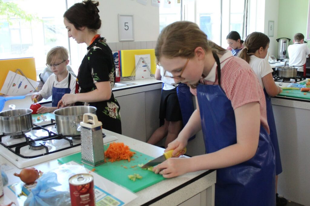 A student chops vegetables. And another is helped by a teacher.